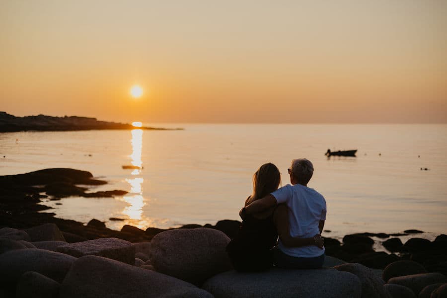 A couple watching the sun set from the rocky Cape Ann shore